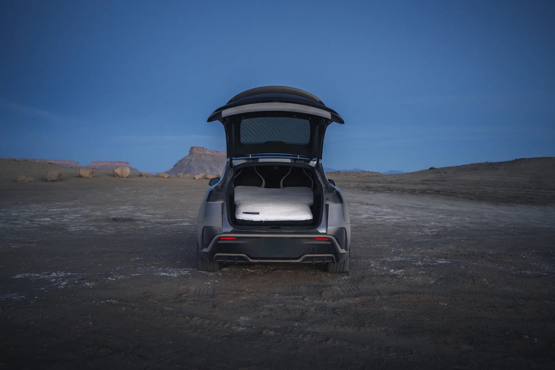 Open rear hatch with a white mattress at a desert campsite