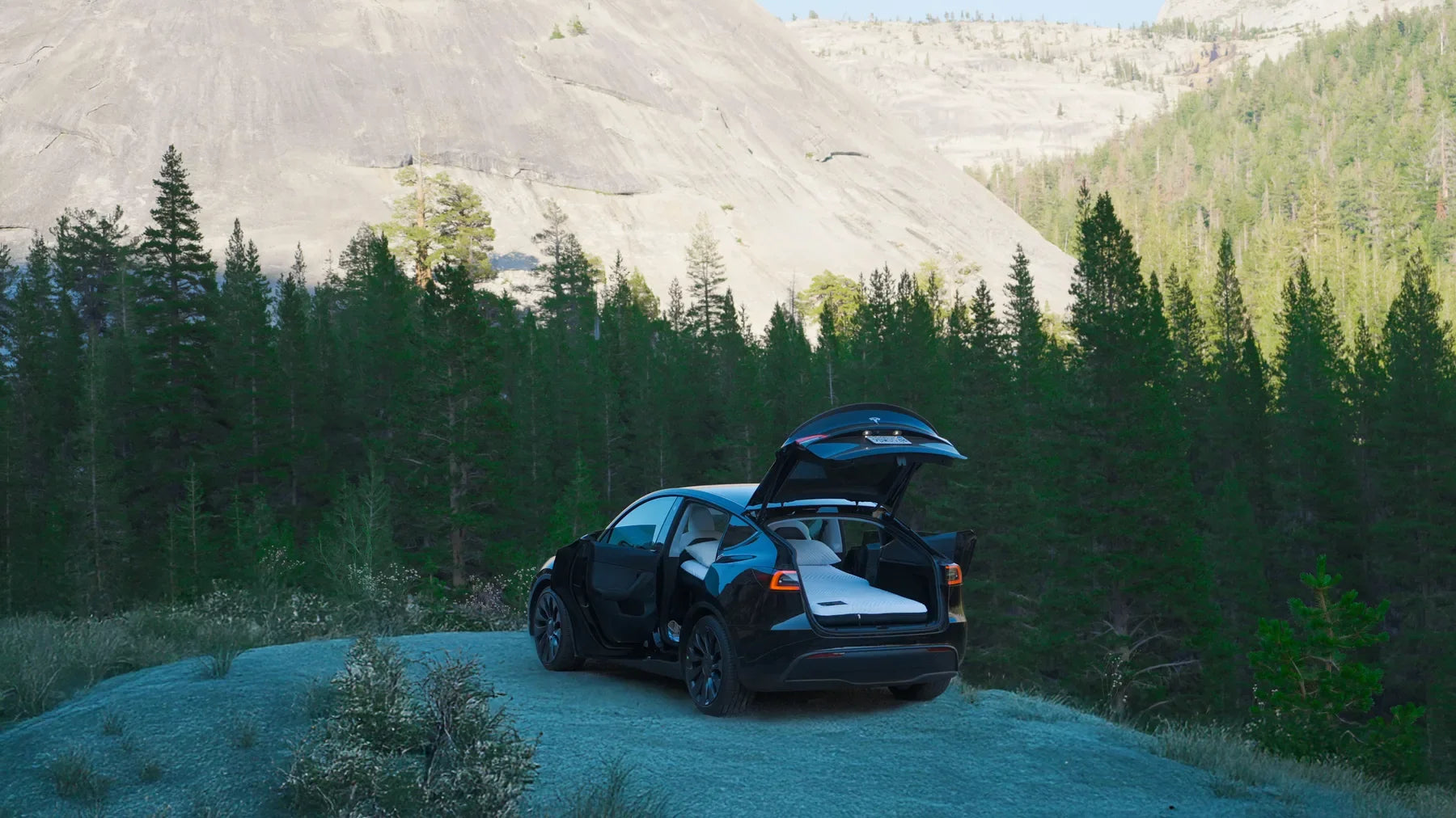Tesla with open doors, raised hatch and a prepared bed at a mountain overlook