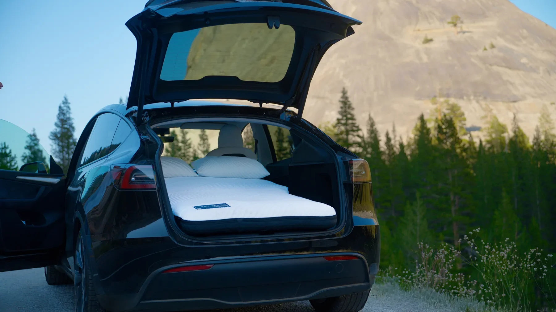 White mattress and pillows inside an open Tesla at a mountain campsite
