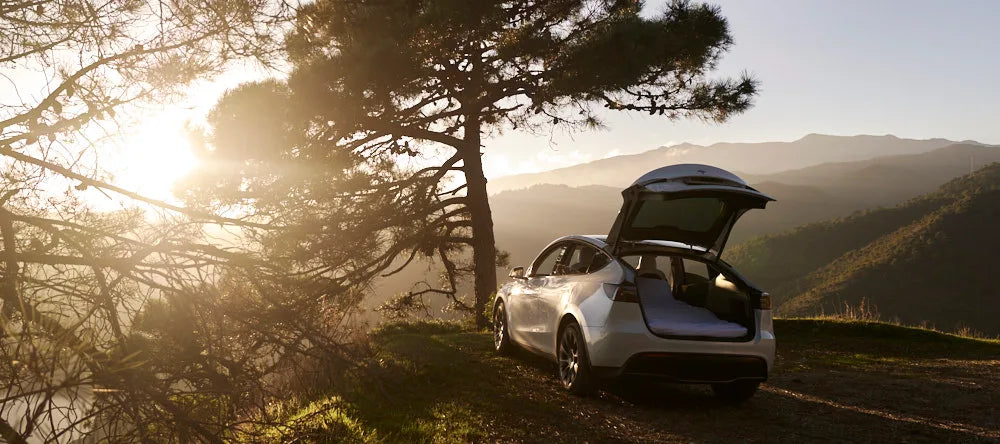 Open Tesla with a prepared rear mattress in a sunlit mountain landscape